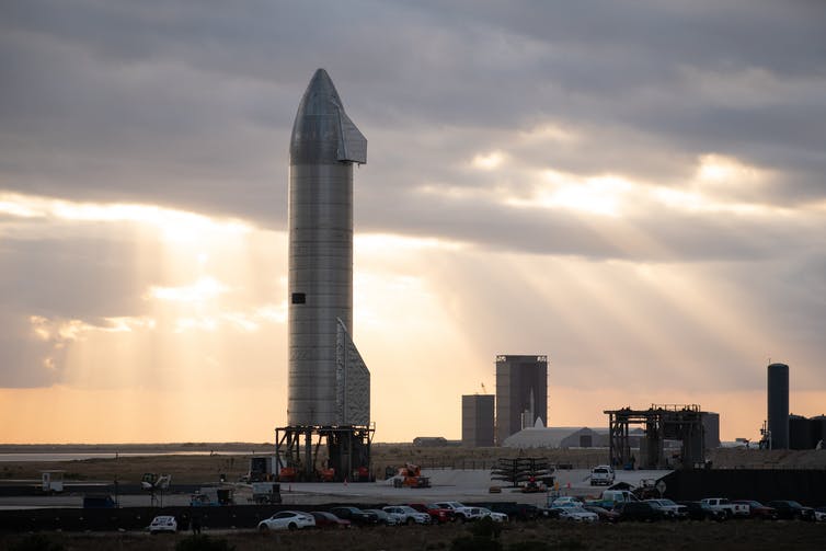 A large silvery rocket standing upright on a launchpad.