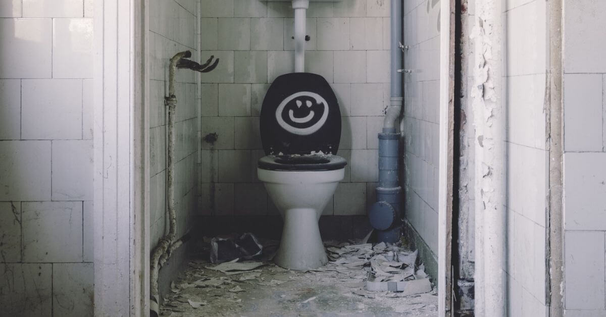 A photograph of a bathroom stall. A smiley face is painted on the toilet lid.