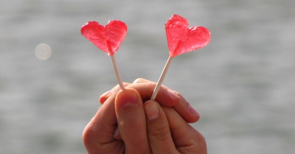 A hand holding two heart-shaped lollypops