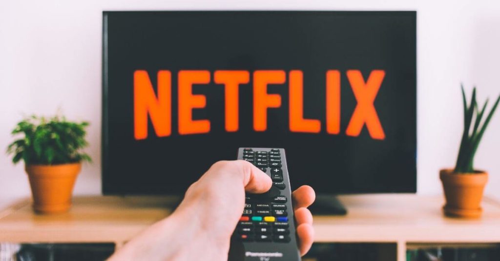 A photo of a hand holding a remote pointing it at a TV with Netflix on it