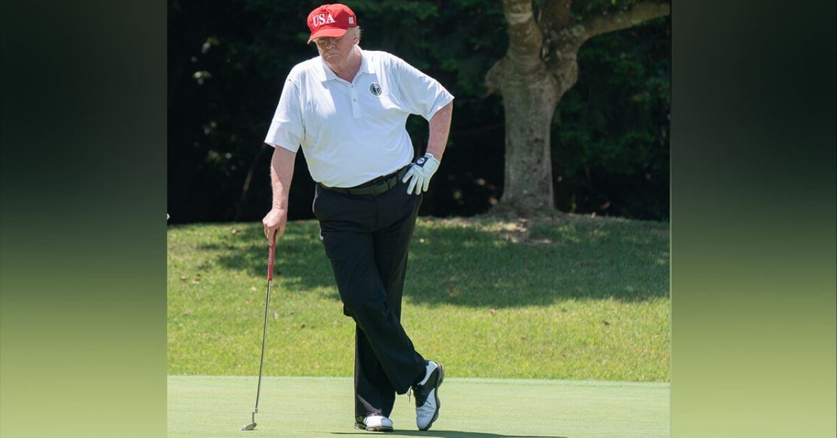 Donald Trump on a golf course leaning on a club.