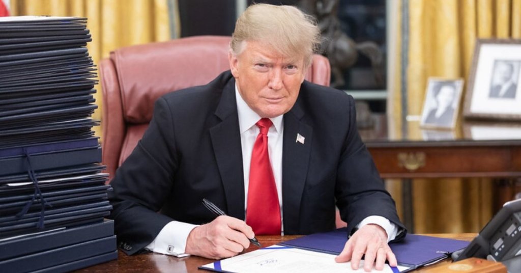 Donald Trump sitting at a desk signing legislation