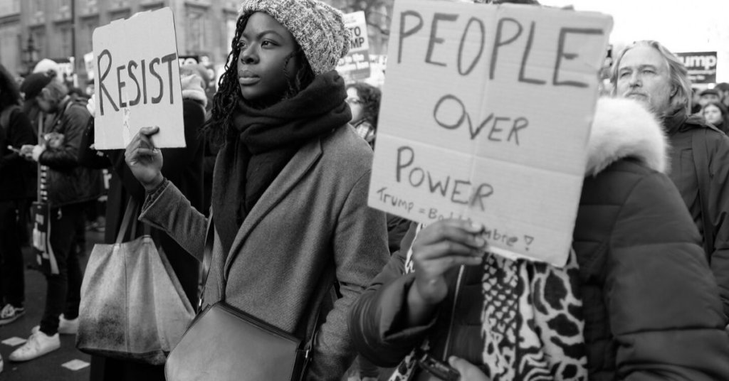 African American protestors holding signs that say Resist and People Over Power