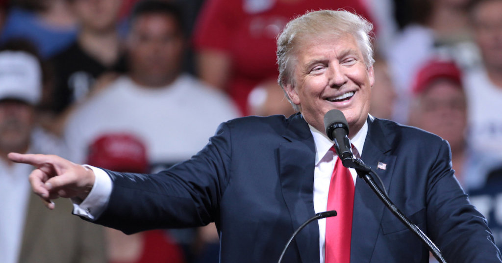 A photograph of Donald Trump on a rally platform smiling and pointing.