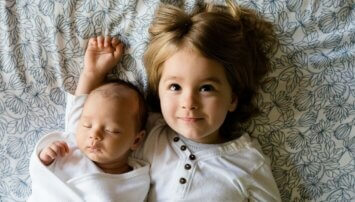 A small child and a baby laying on a blanket