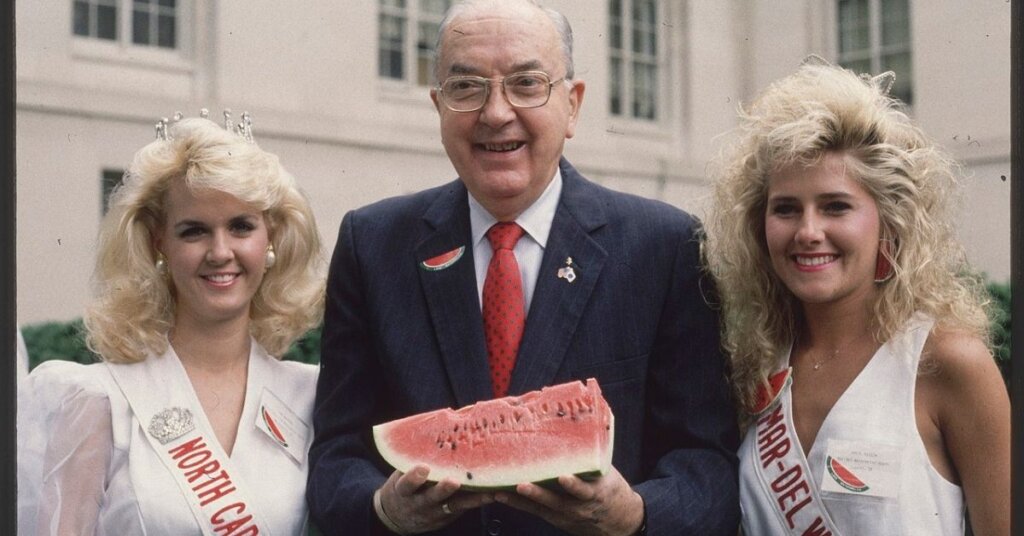 Jesse Helms holding a watermelon standing between two women