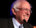 Sanders smiling while standing in front of a microphone
